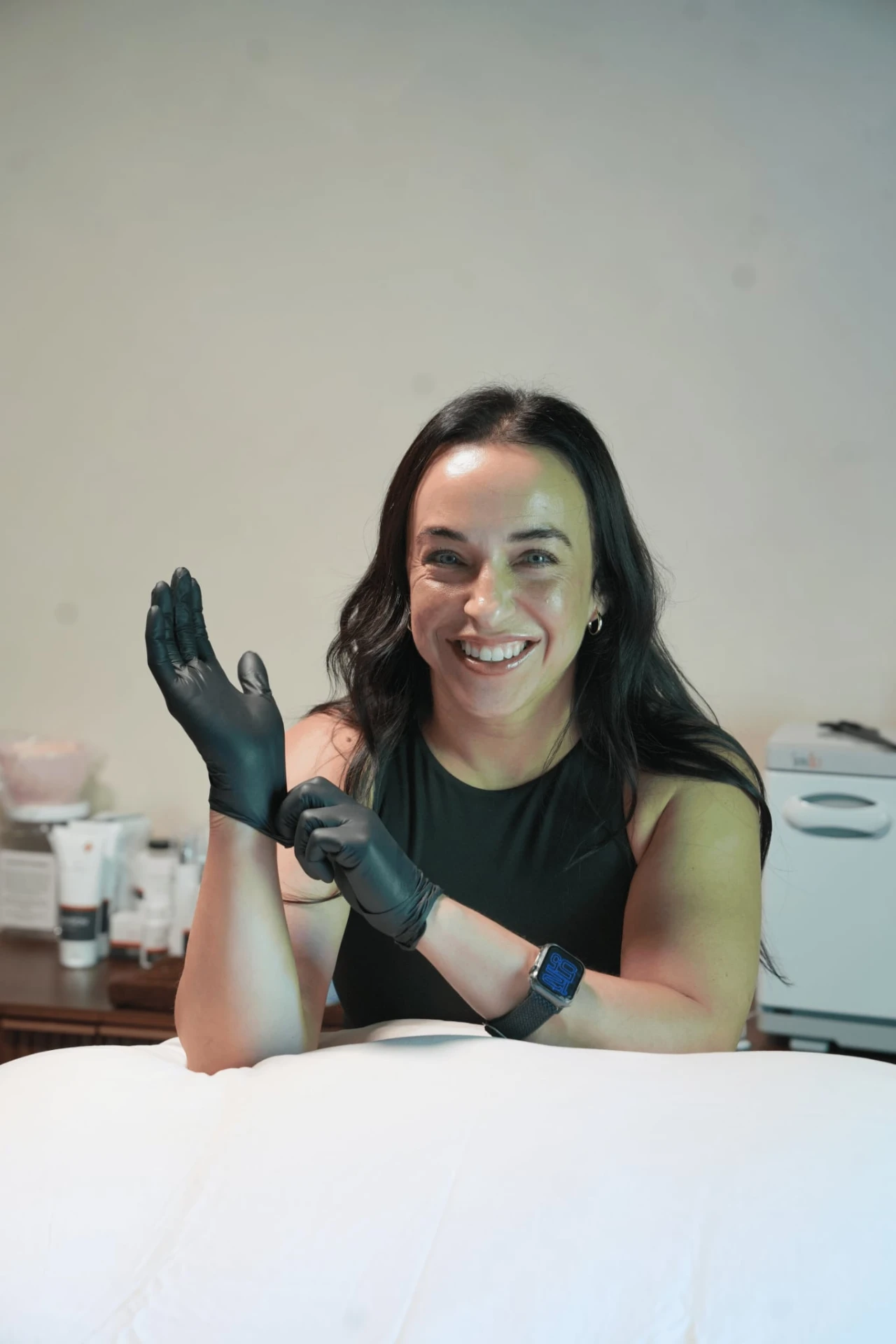 A smiling provider in black gloves preparing for treatment in a clean clinical room.